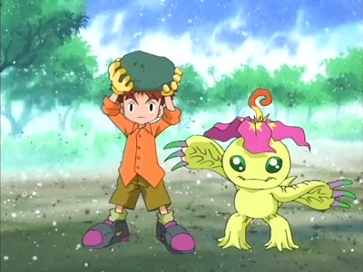 The wall has broken away to reveal Palmon and Koushirou holding up a rock roughly the size of his head, implying he helped break the wall down with this implement.